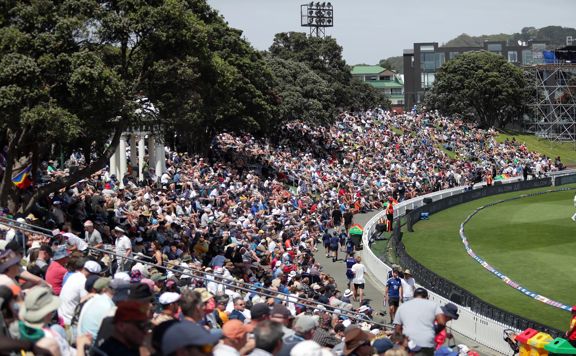 Crowds of people sit on the bank at the Cello Basin Reserve watching a cricket game.