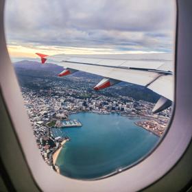 View out of Aeroplane  window of Wellington Harbour, with blue ocean water, colourful sunset and clouds.