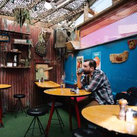 The rustic outdoor dining area of Fidels with a  customer sitting down and drinking.