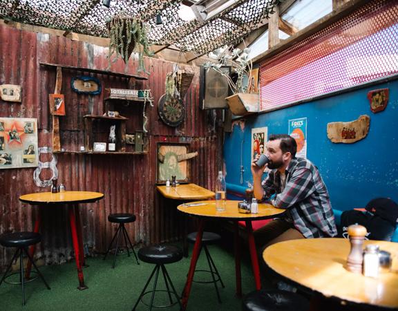 The rustic outdoor dining area of Fidels with a  customer sitting down and drinking.