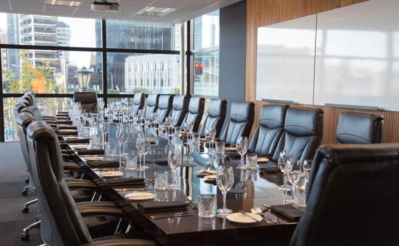 A conference room with a huge table, set with dinner-wear and big leather office chairs.