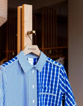 A blue striped button up made by KowTow is hung on a gold hook.