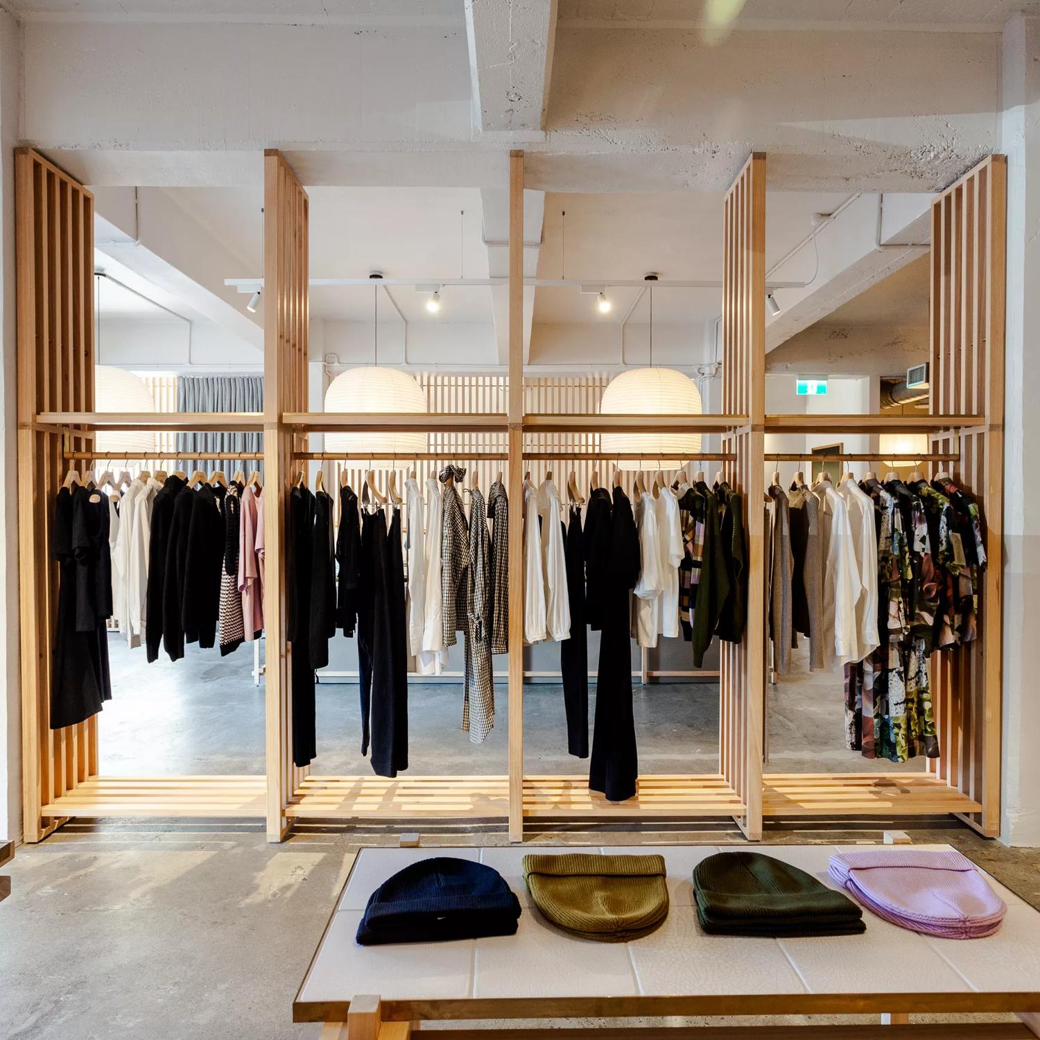 The minimalistic interior of Kowtow, wooden slats holding up hangars of clothes in the centre and beanies sitting on a table in the foreground.