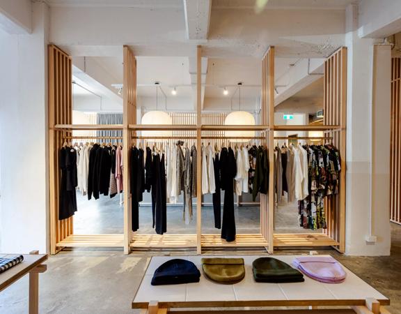 The minimalistic interior of Kowtow, wooden slats holding up hangars of clothes in the centre and beanies sitting on a table in the foreground.