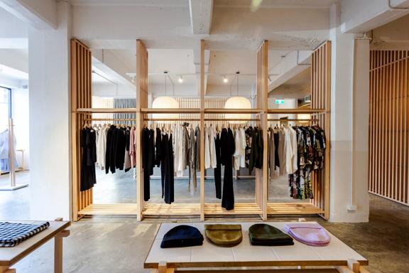 The minimalistic interior of Kowtow, wooden slats holding up hangars of clothes in the centre and beanies sitting on a table in the foreground.