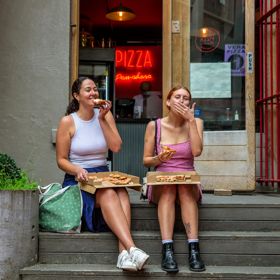 Two people sitting on the front steps of Pizza Pomodoro eating pizza.