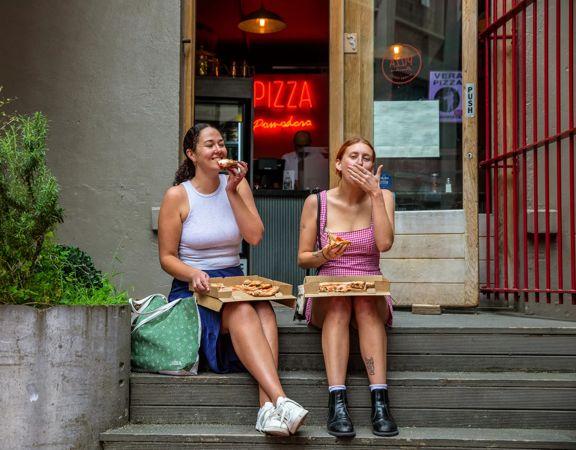 Two people sitting on the front steps of Pizza Pomodoro eating pizza.