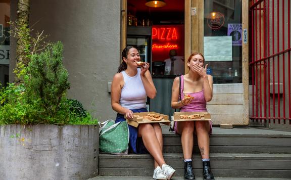 Two people sitting on the front steps of Pizza Pomodoro eating pizza.