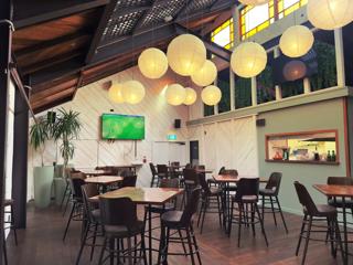 Inside an empty restaurant. There are seven high-top tables with four bar stools at each, a television on the wall with a football match on and spherical paper lanterns suspended from above.