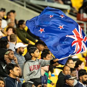 New Zealand flag waving above a packed stadium crowd.
