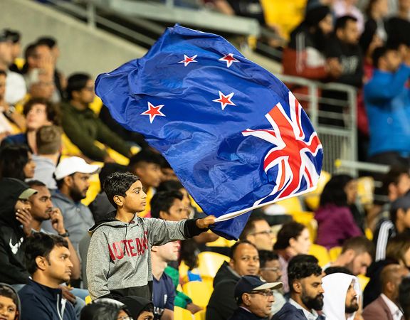 New Zealand flag waving above a packed stadium crowd.