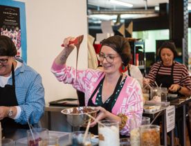 People are making their own chocolate bars at Wellington Chocolate Factory. A person is using a spatula to mix melted chocolate in a silver bowl.