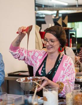 People are making their own chocolate bars at Wellington Chocolate Factory. A person is using a spatula to mix melted chocolate in a silver bowl.