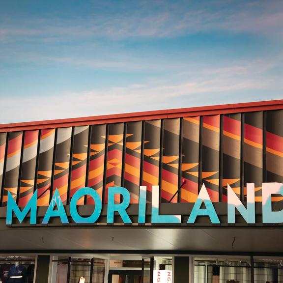 Image of Maoriland signage on top of a building. Large blue letters against textured orange and brown roof cladding.