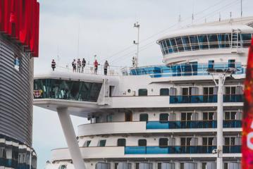 A cropped image of the top four floors of a massive cruise ship with six people standing on the top deck.