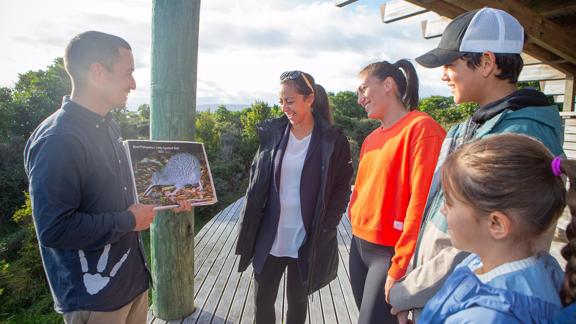 A tour guide telling a group of people about the Kiwi, while holding up a picture.