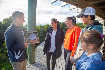 A tour guide telling a group of people about the Kiwi, while holding up a picture.