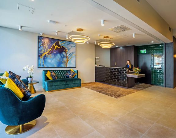The Sebel Thorndon's lobby. A worker is behind reception desk. Furnishings are teals and blues.