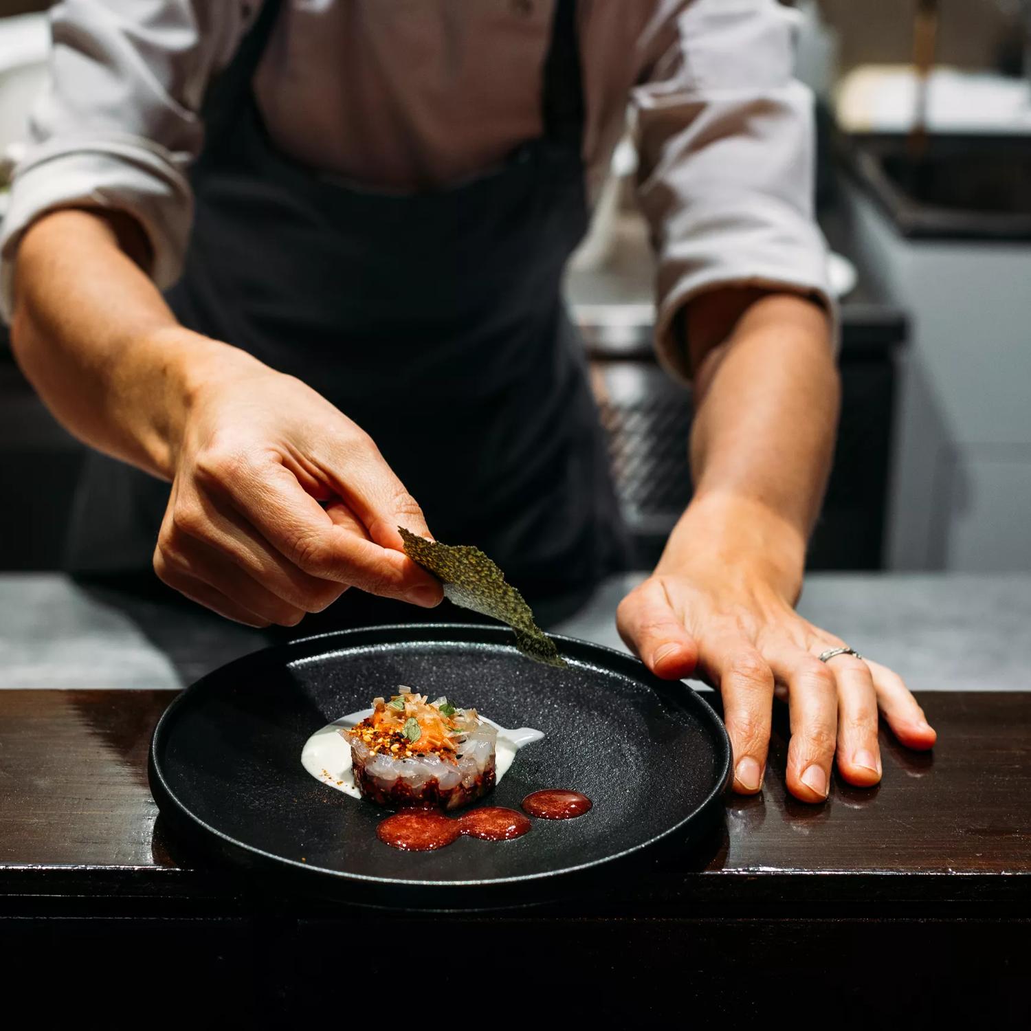 Close-up of chef finishing plating food at 50-50 restaurant at Paraparaumu Beach.