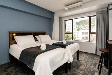 Inside a private room in Haka House on Wakefield Street. Two beds sit side by side in the room with a desk and wardrobe, and a view of Mount Victoria out the window.