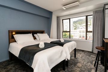 Inside a private room in Haka House on Wakefield Street. Two beds sit side by side in the room with a desk and wardrobe, and a view of Mount Victoria out the window.