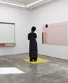 Person standing on a yellow square at PEG Gallery looking at minimalist artwork on a wall.
