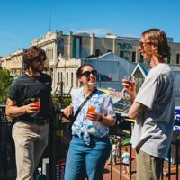 Three friends enjoy the sunshine, cocktails and conversation on the balcony at Regent on the corner of Cuba Street and Guhznee Street in Te Aro Wellington.