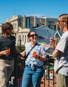 Three friends enjoy the sunshine, cocktails and conversation on the balcony at Regent on the corner of Cuba Street and Guhznee Street in Te Aro Wellington.