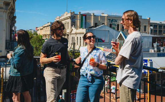 Three friends enjoy the sunshine, cocktails and conversation on the balcony at Regent on the corner of Cuba Street and Guhznee Street in Te Aro Wellington.