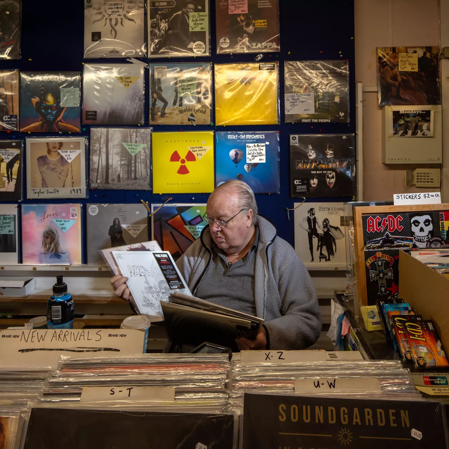 A man sits behind the counter looking through a stack of vinyls at Lo-Cost / Moonhop, a music store in Petone, Lower Hutt, New Zealand.