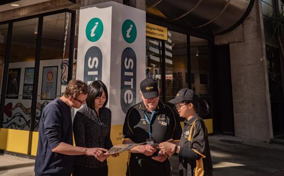 Two City Ambassadors are helping two tourists outside the isite Visitor Information Centre located near the waterfront in Te Aro Wellington. 