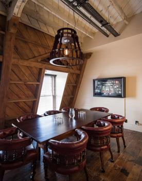 In the Capital Room inside the Wellington Museum, 8 leather armchairs sit around a dark wooden table, and a slanted wooden ceiling holds up a rustic chandelier.