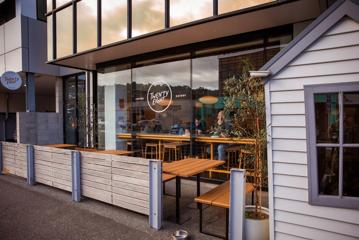 The exterior of Twenty Eight, a café in Lower Hutt. A few patrons are visible through the glass facade and three picnic tables are on the patio.