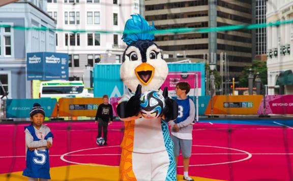Tazuni the penguin holds a football at the Fifa unity Pitch.