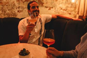 A person wearing a white shirt sits at a booth table drinking a glass of wine at Puffin Wine Bar in Wellington.