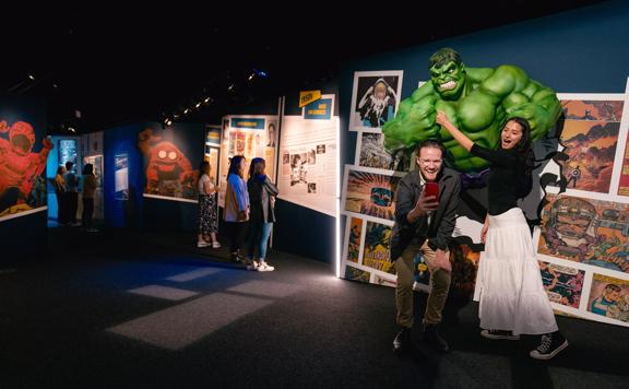 Two people posing and taking a selfie with The Incredible Hulk statue at Marvel: Earth's Mightiest Exhibition at Tākina.