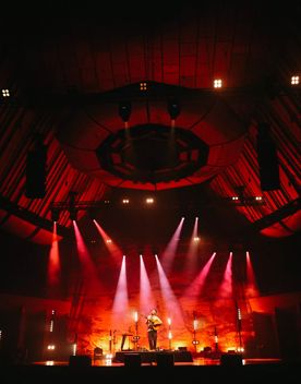 Ziggy Alberts plays guitar on stage under red spotlights at Michael Fowler Centre in Wellington.