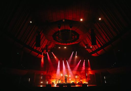 Ziggy Alberts plays guitar on stage under red spotlights at Michael Fowler Centre in Wellington.
