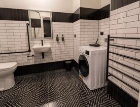 A black and white accessible bathroom at the Tryp by Wyndham has plenty of space around the fixtures with the basin sitting low and front loading washing machine.