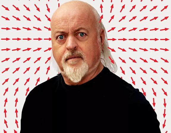 Mid shot of musician and comedian Bill Bailey in front of a white background filled with little red arrow icons, pointing in multiple directions.