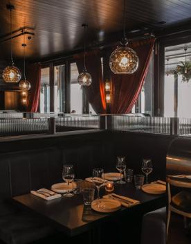 A booth table set  for four with plates and wine glasses and amber lighting inside Foxglove Bar and Restaurant located on the waterfront at 33 Queens Wharf, Wellington Central.