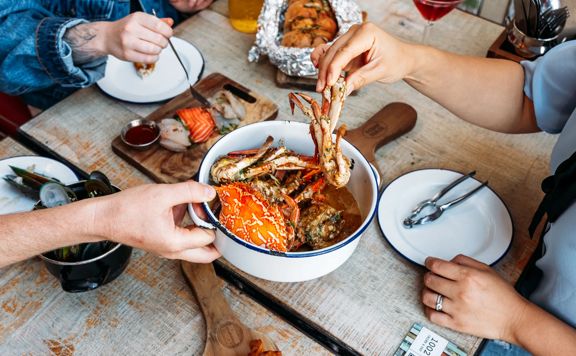 Three people eat crab and other seafood plates at The Crab Shack on Queens Wharf.