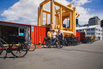 A staff member at Switched On Bikes demonstrates an e-bike to two visitors outside their vibrant orange, converted shipping container office.