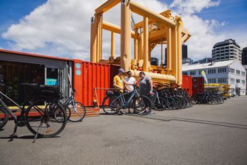 A staff member at Switched On Bikes demonstrates an e-bike to two visitors outside their vibrant orange, converted shipping container office.