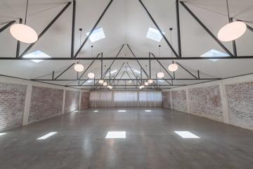 The interior of Whisky and Wood, an event venue in Wellington Central. It's a large empty room with cement floors, exposed brick walls, a white curtain covering three windows at the back of the space, and a cathedral ceiling with eight skylights.