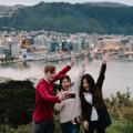 Three people are taking a selfie at the Mount Victoria Lookout with a view of Wellington harbour and city centre behind them.