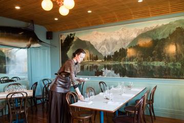 Waiter setting a table inside Ortega Fish Shack. A large Marlin is mounted on one wall and a very large painting of a lake is on the other.