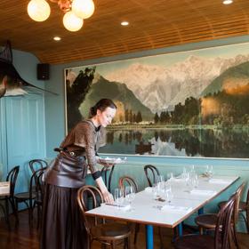 Waiter setting a table inside Ortega Fish Shack. A large Marlin is mounted on one wall and a very large painting of a lake is on the other.