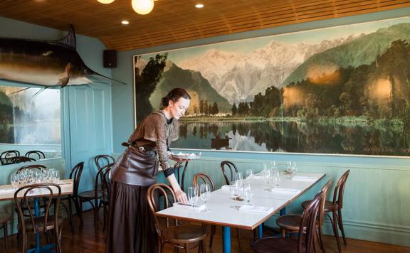 Waiter setting a table inside Ortega Fish Shack. A large Marlin is mounted on one wall and a very large painting of a lake is on the other.