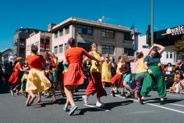 Dancers in colourful clothes pair up, hold hands and skip in circles.